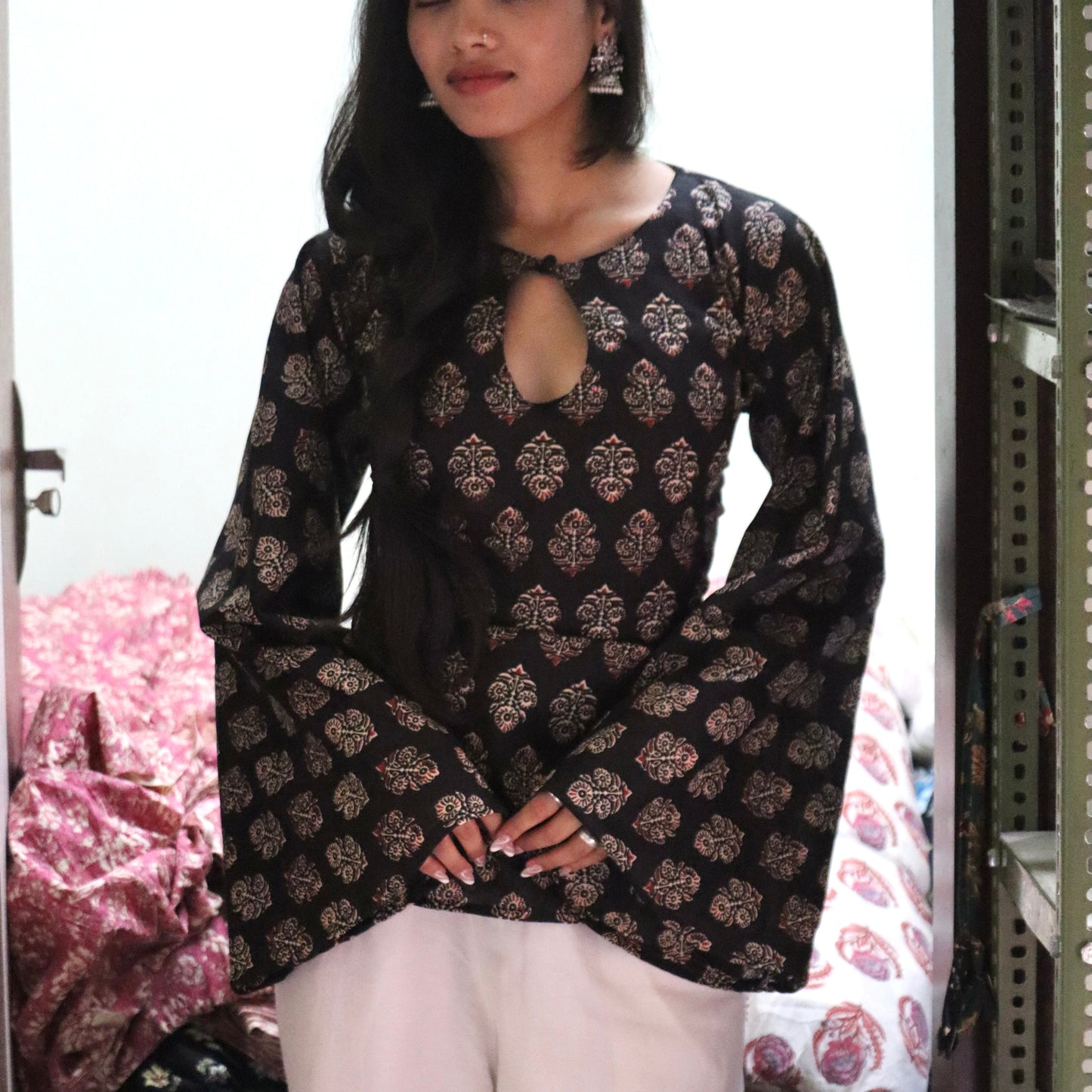 Woman wearing a black patterned top and white pants in a store setting.