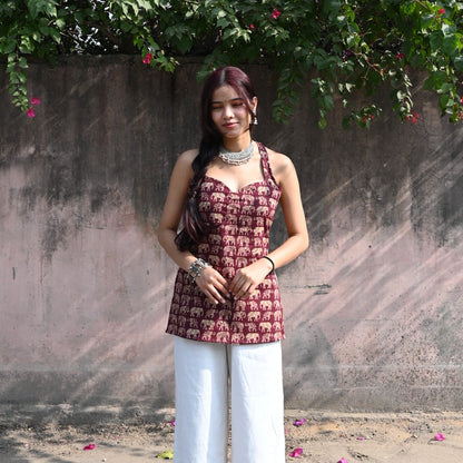 Woman in a patterned top and white pants standing under a tree with pink flowers.