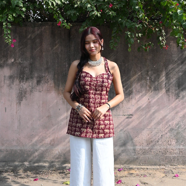 Woman in a patterned top and white pants standing under a tree with pink flowers.