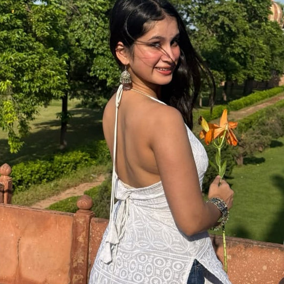 Woman in a white dress standing outdoors with trees and a path in the background